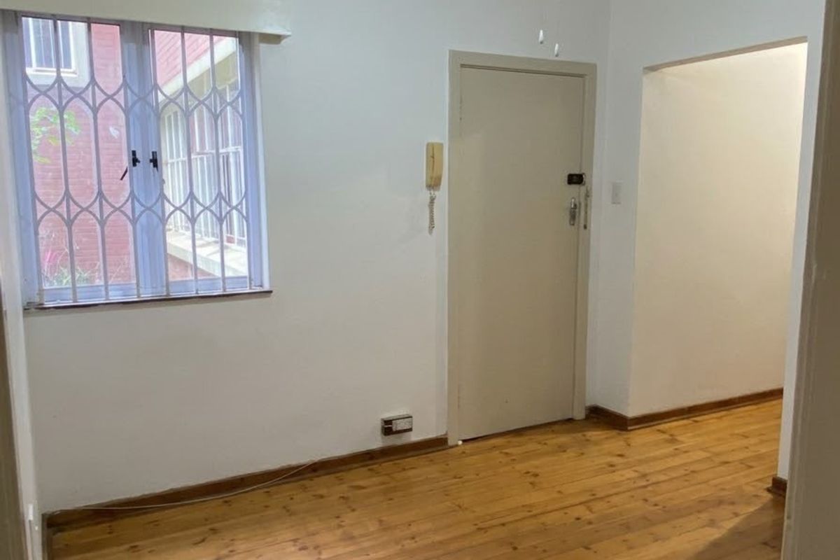 An empty bedroom featuring original hardwood flooring, a ceiling fan, and a window fitted with a security gate.