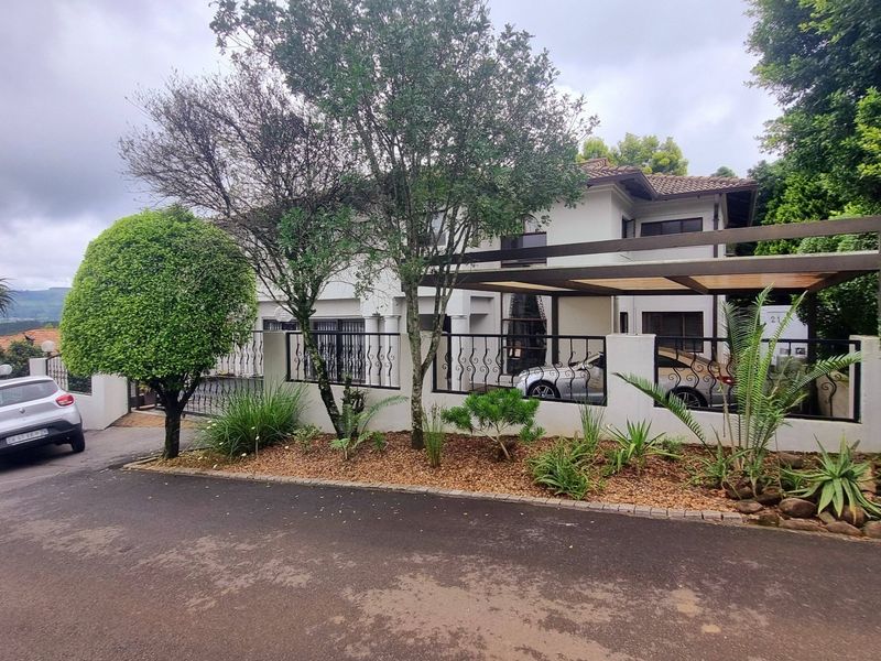 Front elevation of a two-story house featuring a paved driveway, carport, wrought iron fencing, and a well-maintained landscaped garden.