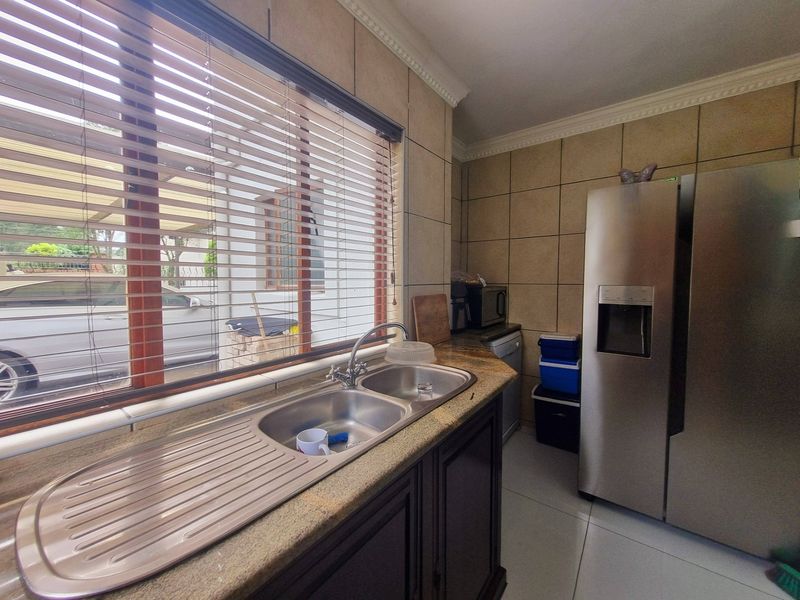 A functional kitchen featuring granite countertops, a double bowl stainless steel sink, tiled wall finishes, and large windows with venetian blinds.