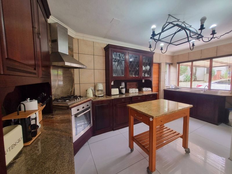 A well-appointed kitchen featuring dark wood cabinetry, granite countertops, a gas hob with extractor, and tiled flooring, offering a classic and functional workspace.