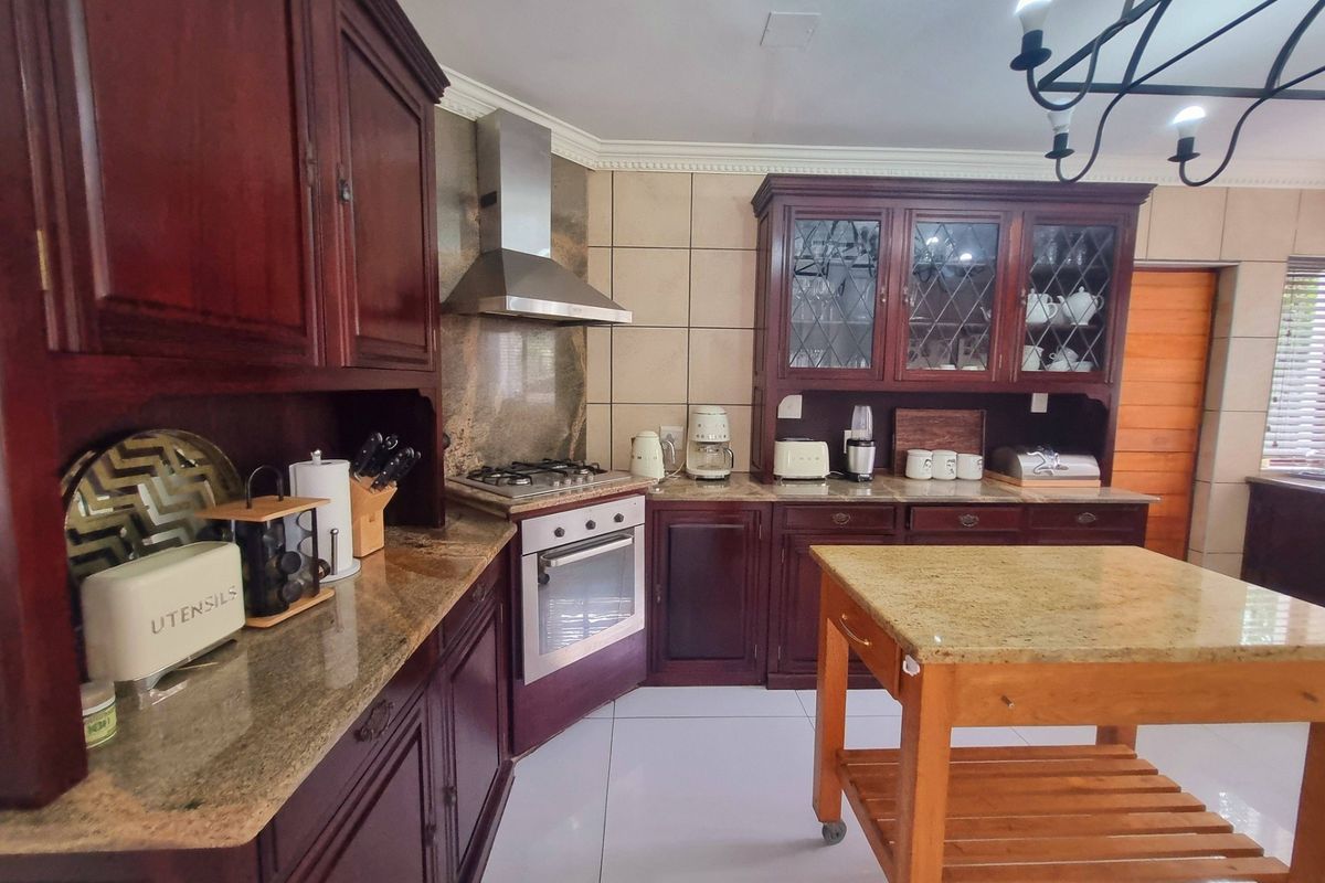 Traditional kitchen featuring dark wood cabinetry, granite countertops, a gas hob with stainless steel extractor, and tiled finishes throughout.