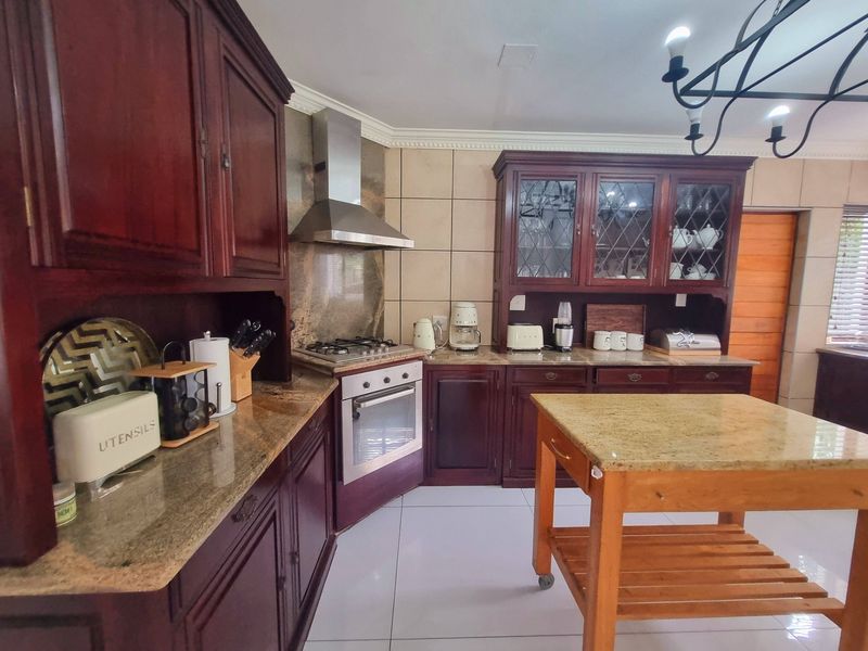 Traditional kitchen featuring dark wood cabinetry, granite countertops, a gas hob with stainless steel extractor, and tiled finishes throughout.
