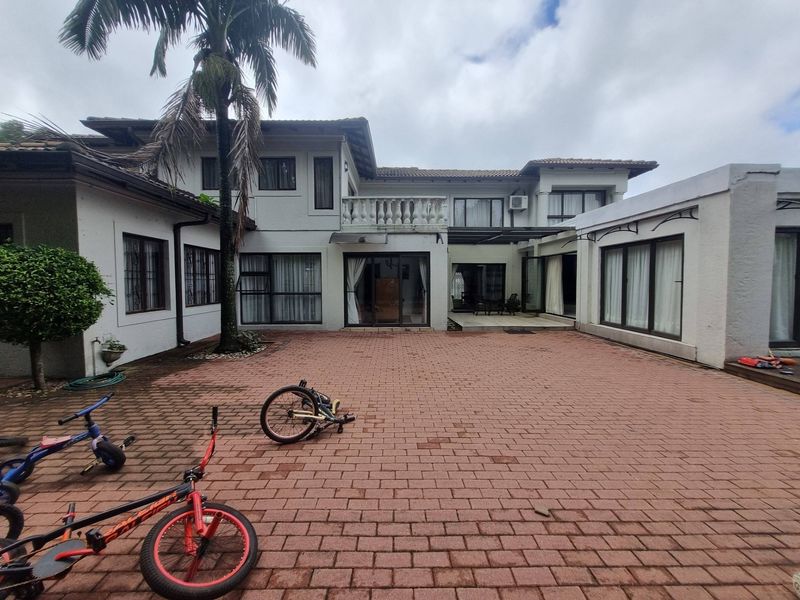 Spacious rear courtyard featuring paved flooring, multiple access points via sliding glass doors, and an upper-level balcony with a classic balustrade.