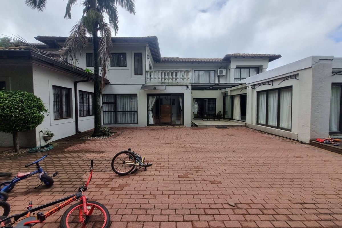 Spacious rear courtyard featuring paved flooring, multiple access points via sliding glass doors, and an upper-level balcony with a classic balustrade.