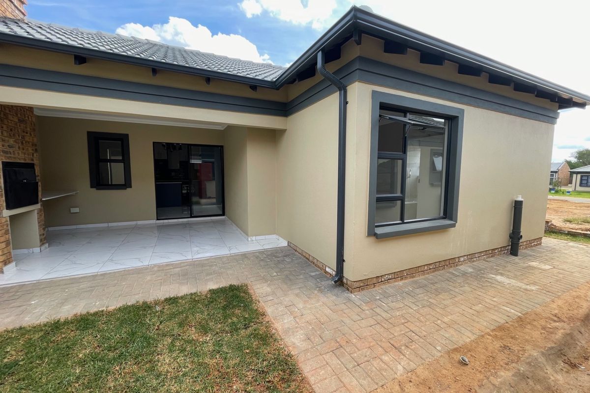 Rear view of the property featuring a covered patio with a built-in braai, tiled flooring, and paved outdoor area.
