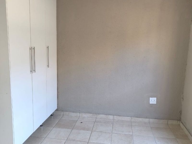 An empty bedroom featuring neutral tiled flooring, built-in white cupboards, and a simple light fixture.