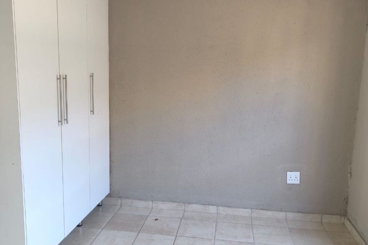 An empty bedroom featuring neutral tiled flooring, built-in white cupboards, and a simple light fixture.