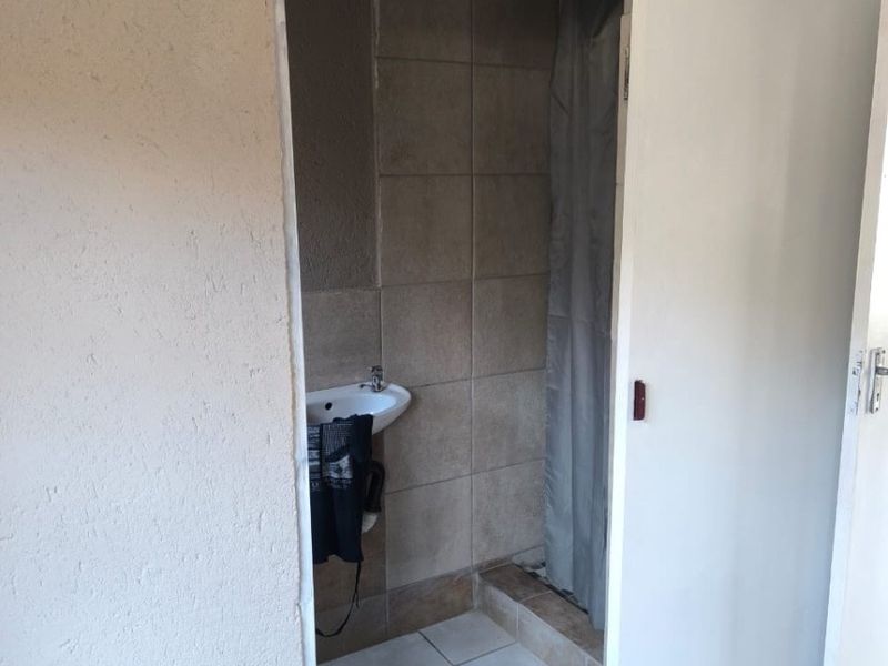 A compact bathroom featuring a wall-mounted basin and a tiled shower enclosure, currently requiring finishing touches to the wall plaster and door frame.