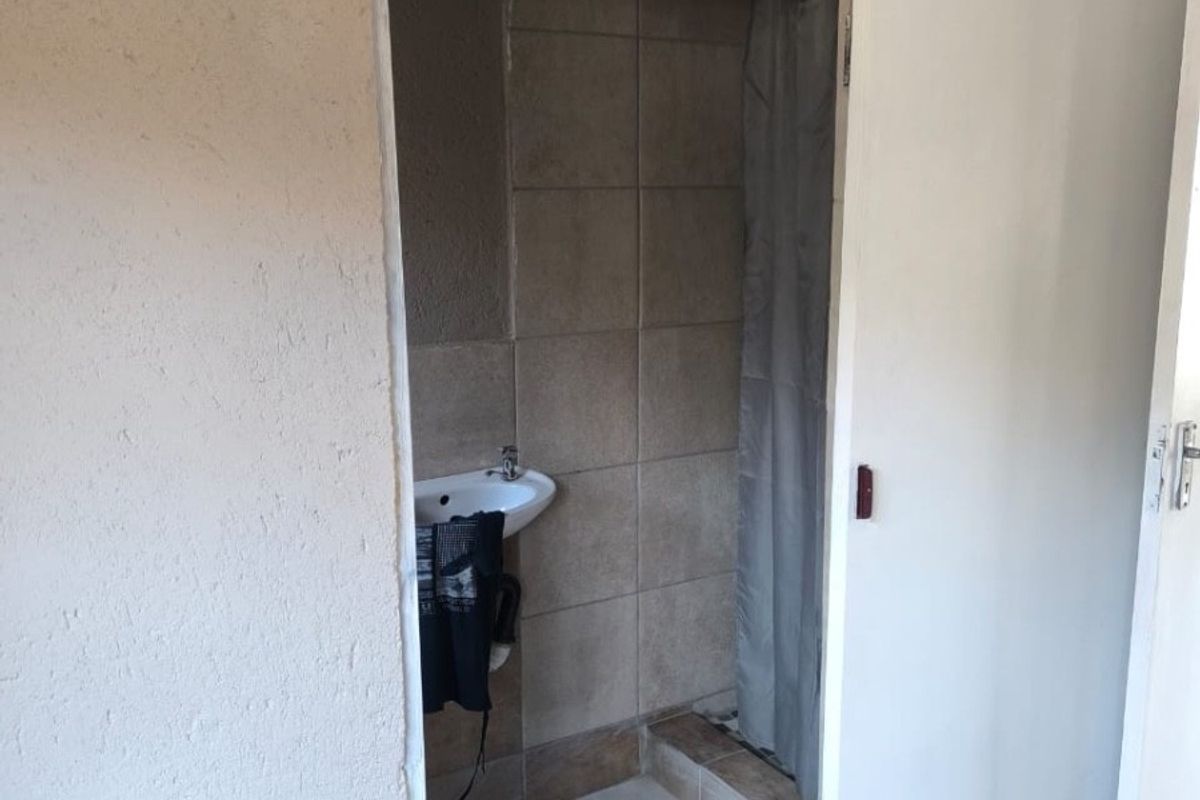 A compact bathroom featuring a wall-mounted basin and a tiled shower enclosure, currently requiring finishing touches to the wall plaster and door frame.