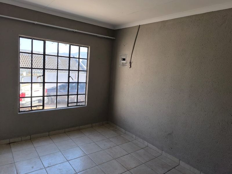 An empty bedroom featuring tiled flooring, a steel-framed window, and unfinished wall surfaces with exposed electrical wiring.