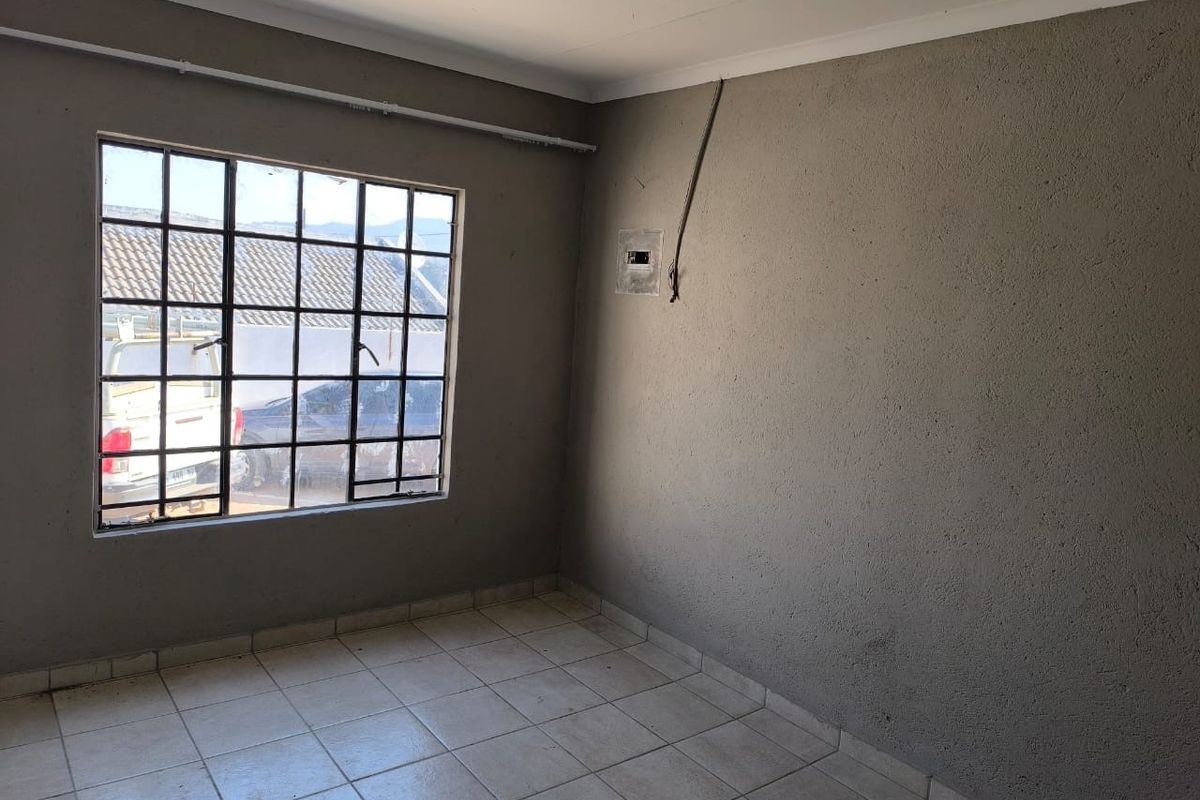 An empty bedroom featuring tiled flooring, a steel-framed window, and unfinished wall surfaces with exposed electrical wiring.