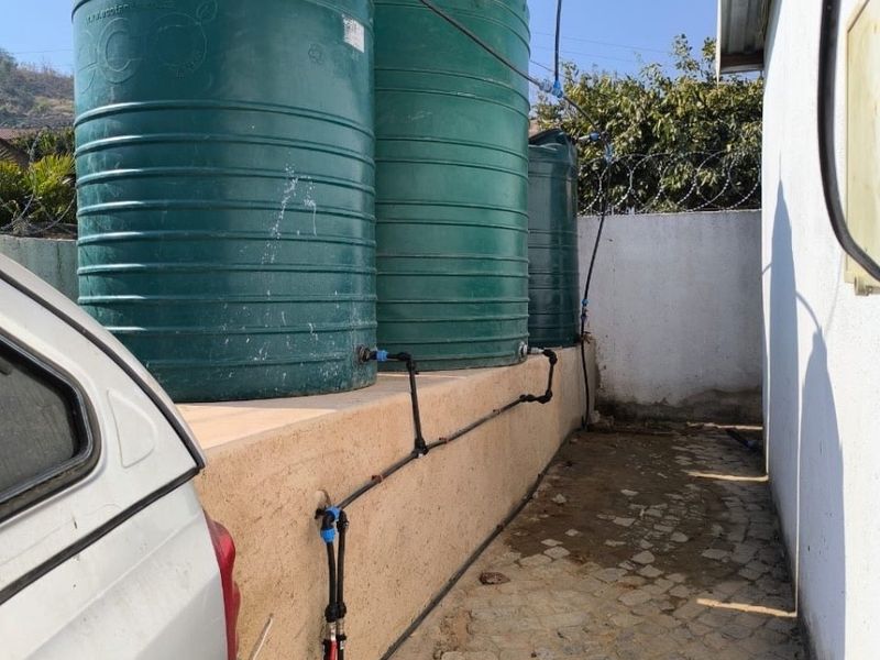 Exterior utility area featuring three large water storage tanks mounted on a raised retaining wall with connected plumbing infrastructure.