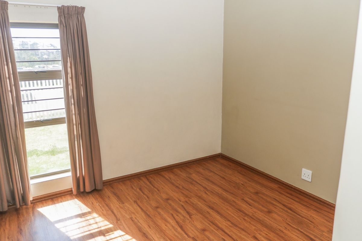 An empty bedroom featuring laminate flooring, a window with security bars, and neutral wall tones, providing a blank canvas for personalization.