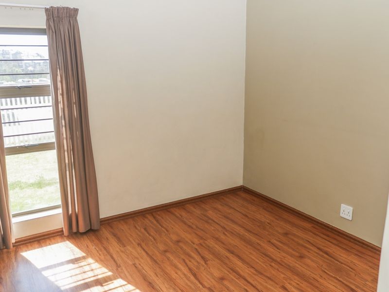 An empty bedroom featuring laminate flooring, a window with security bars, and neutral wall tones, providing a blank canvas for personalization.
