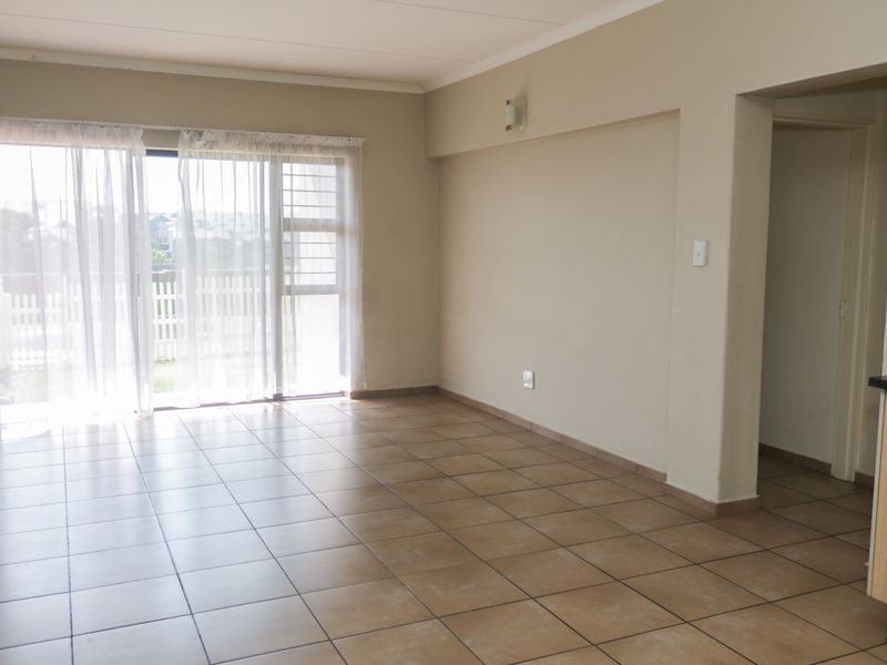 An open-plan living area featuring neutral tiled flooring and a sliding glass door leading to an outdoor space.