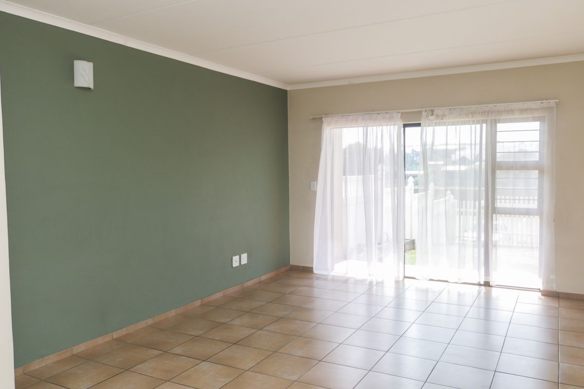 A bright, empty living room featuring neutral tiled flooring, a green accent wall, and a sliding glass door providing access to the exterior.