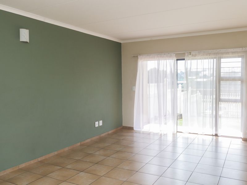 A bright, empty living room featuring neutral tiled flooring, a green accent wall, and a sliding glass door providing access to the exterior.