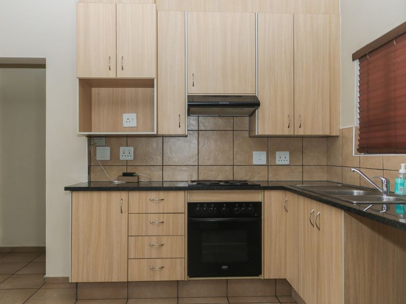 A functional kitchen featuring light wood-finish cabinetry, granite countertops, a built-in oven with hob, and a tiled backsplash.