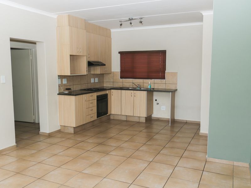 A functional kitchen featuring light wood cabinetry, laminate countertops, built-in oven, hob, extractor fan, and tiled flooring in an open-plan layout.