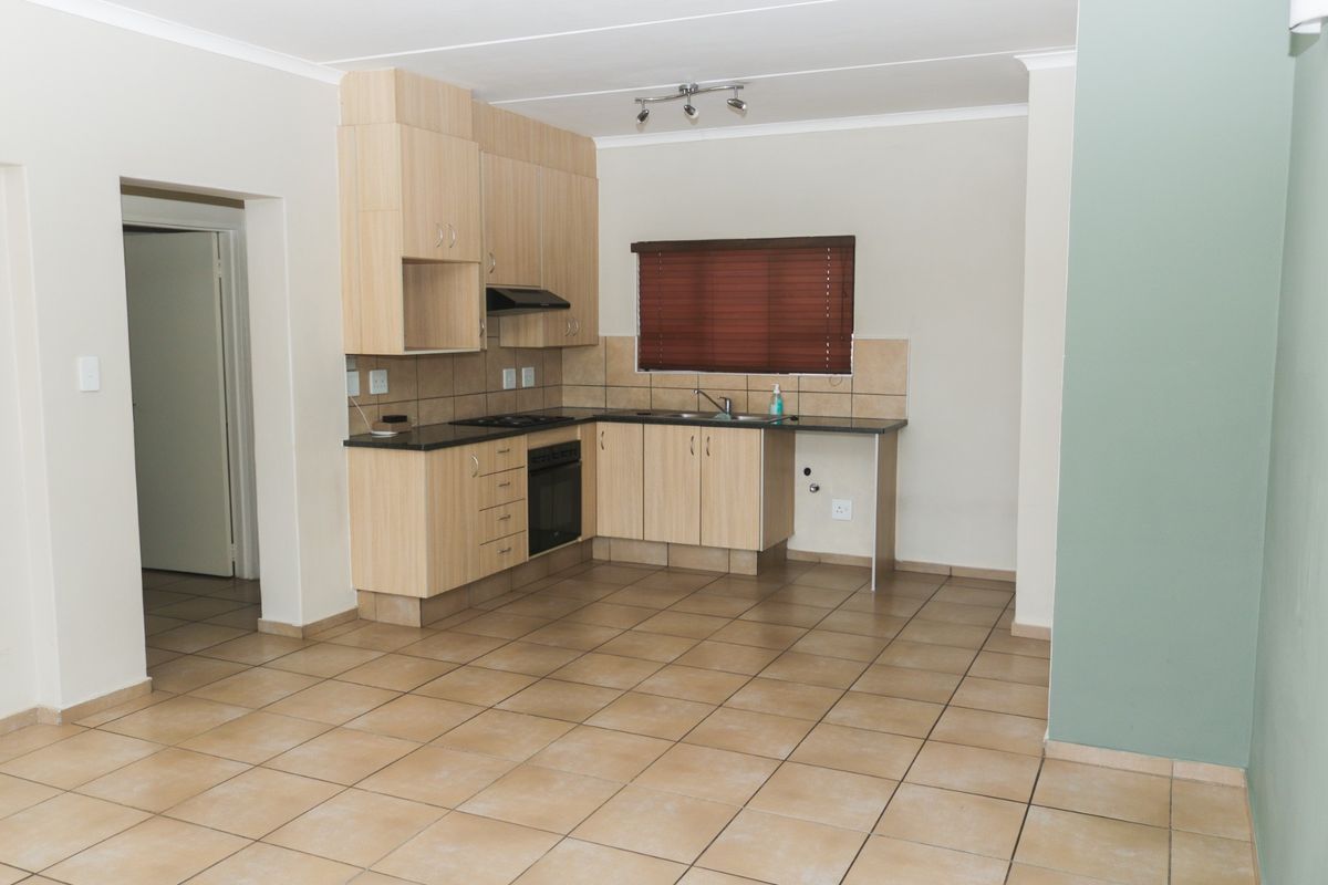 A functional kitchen featuring light wood cabinetry, laminate countertops, built-in oven, hob, extractor fan, and tiled flooring in an open-plan layout.