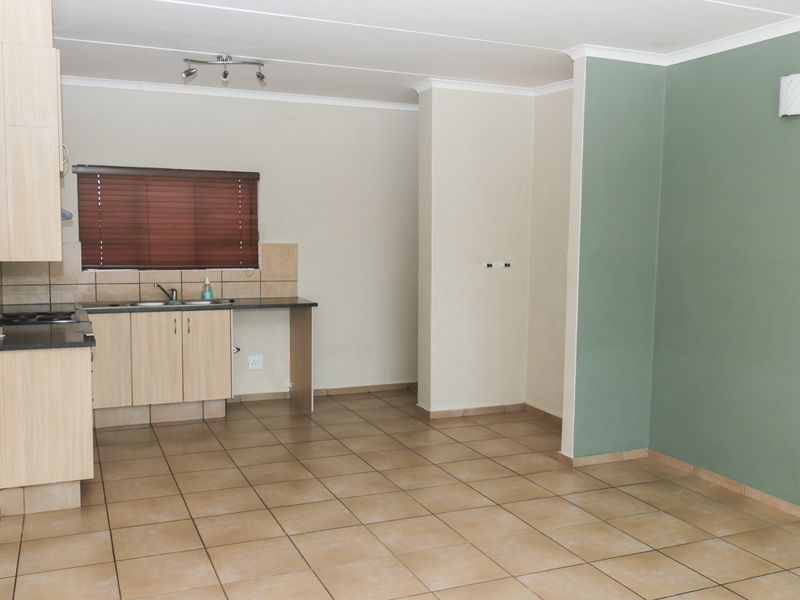 An open-plan living and kitchen area featuring tiled flooring, light wood-finish cabinetry, and a contrasting green accent wall.
