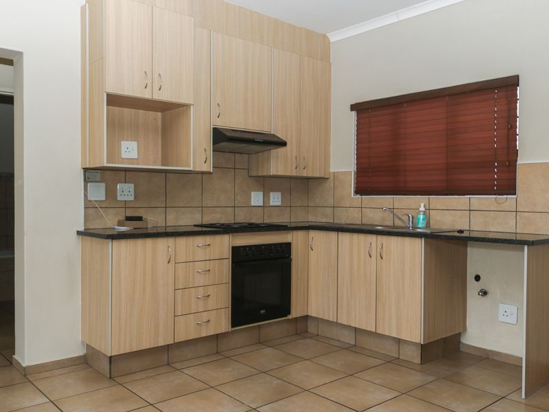 A functional kitchen featuring light wood-finish cabinetry, granite countertops, built-in oven, hob, extractor fan, and tiled flooring with a neutral backsplash.