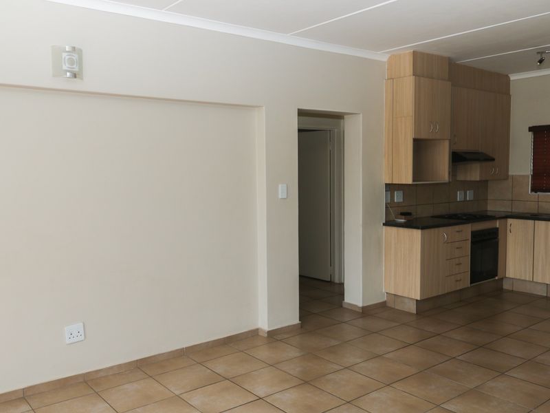 An open-plan living and kitchen area featuring tiled flooring, built-in cabinetry, and integrated kitchen appliances in a neutral, well-maintained space.