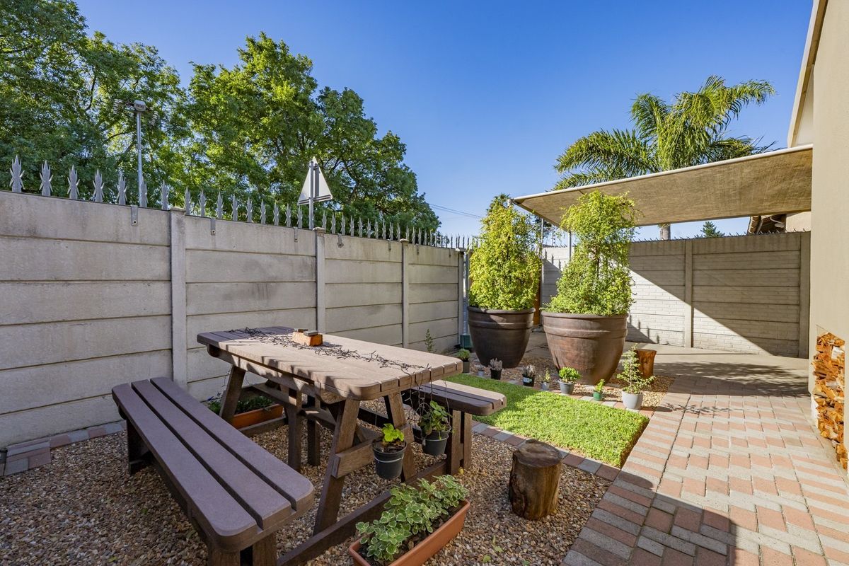 A private rear courtyard featuring a paved patio area, gravel landscaping, and a shade sail, enclosed by a secure precast concrete boundary wall.