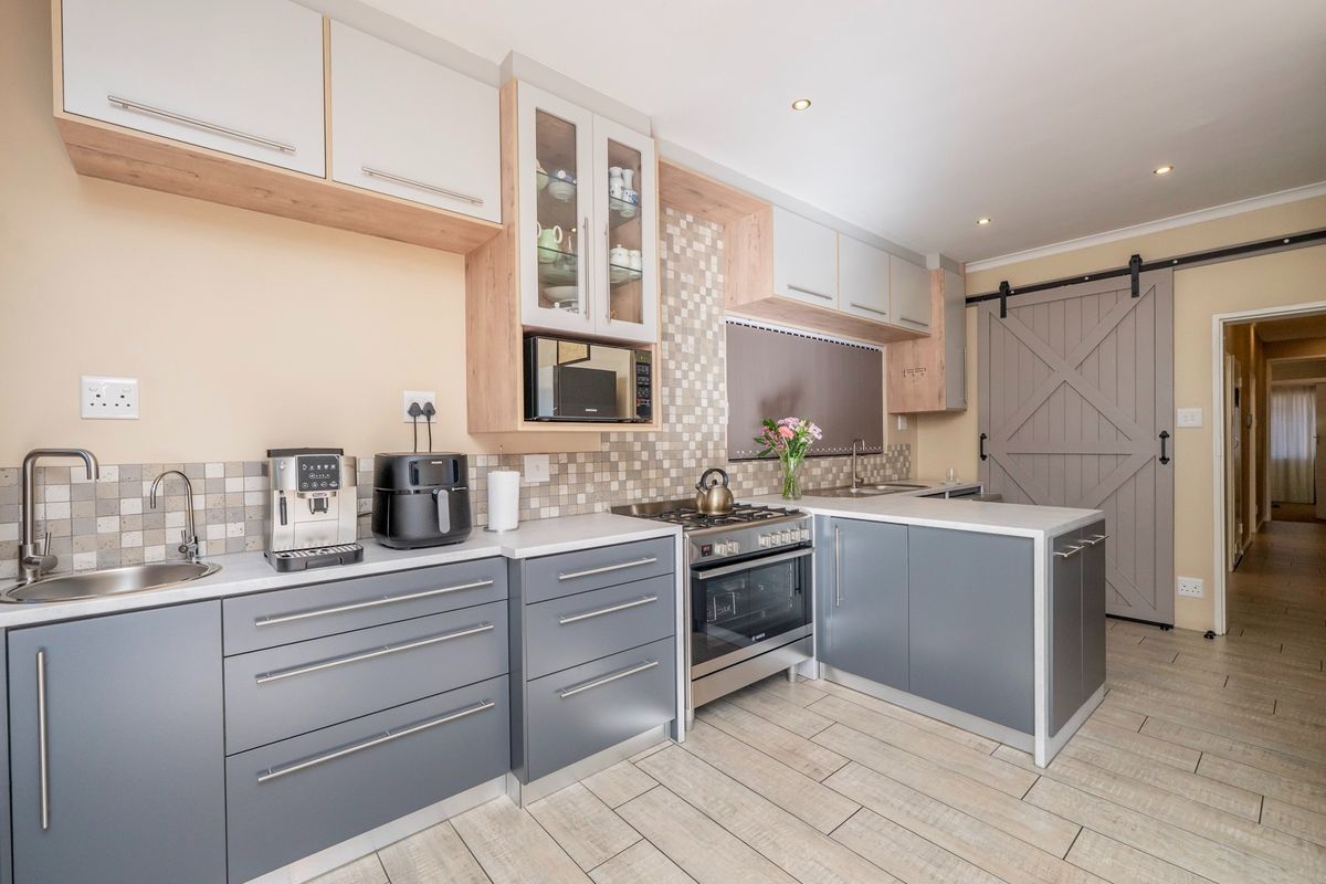 Modern kitchen featuring grey cabinetry, mosaic tile backsplash, stainless steel oven, and a distinctive barn-style sliding door, complemented by light-toned tiled flooring.