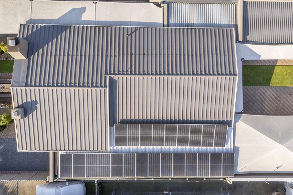 Aerial view of the property showing a well-maintained corrugated metal roof equipped with a large solar panel array and surrounding paved areas.