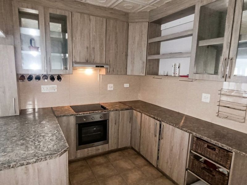 A functional kitchen featuring wood-look laminate cabinetry, stone-effect countertops, built-in oven, electric hob, and tiled flooring with ample storage space.