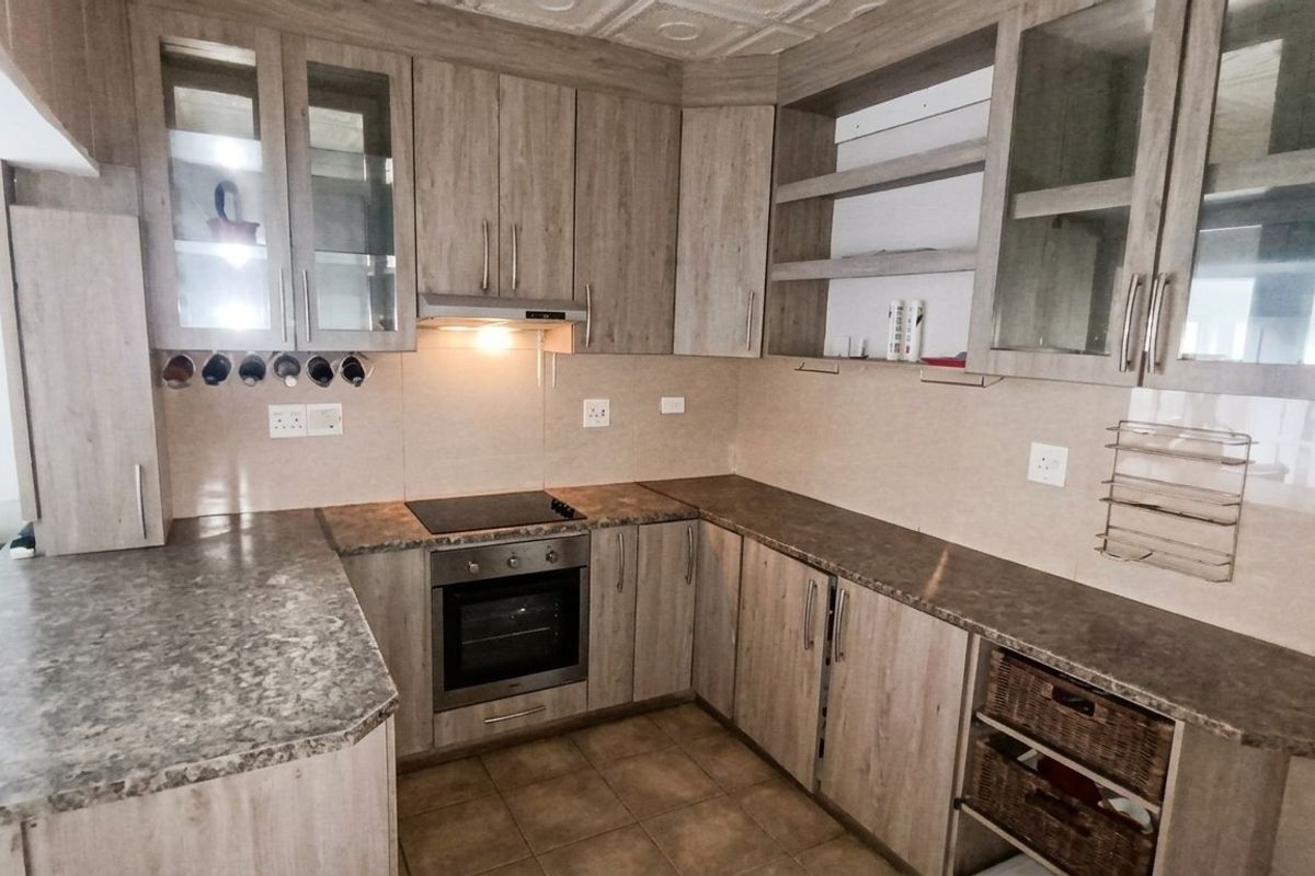 A functional kitchen featuring wood-look laminate cabinetry, stone-effect countertops, built-in oven, electric hob, and tiled flooring with ample storage space.