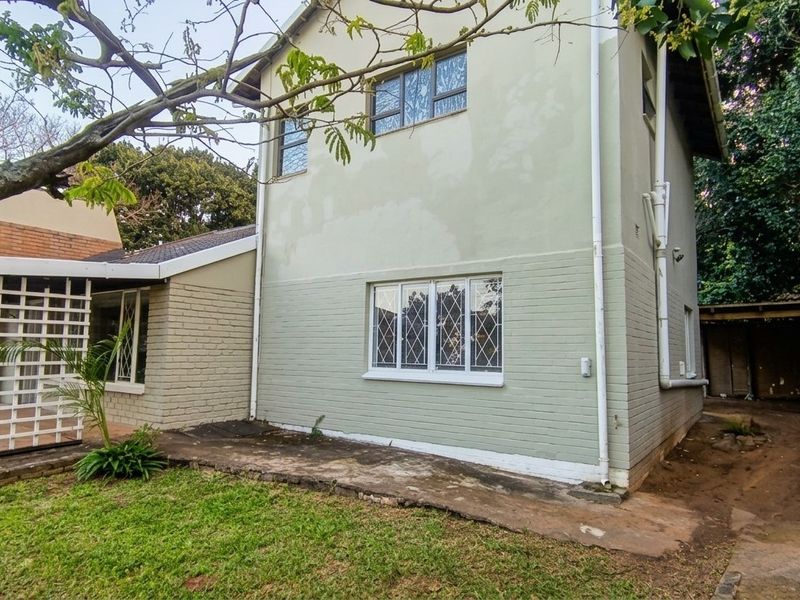 Rear view of the house showing painted brick exterior, security-barred windows, and a concrete pathway leading to the backyard area.