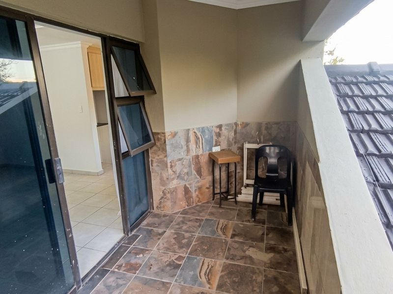 A covered balcony featuring stone wall cladding and tiled flooring, accessible via a sliding glass door, offering a private outdoor space.