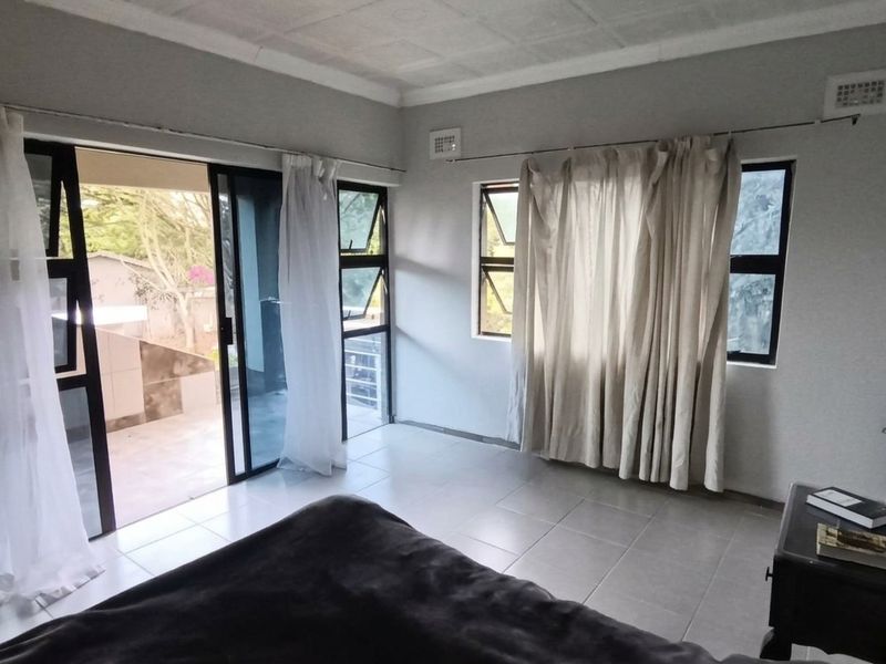 A bedroom featuring tiled flooring, aluminium window frames, and a sliding glass door providing access to an outdoor area.