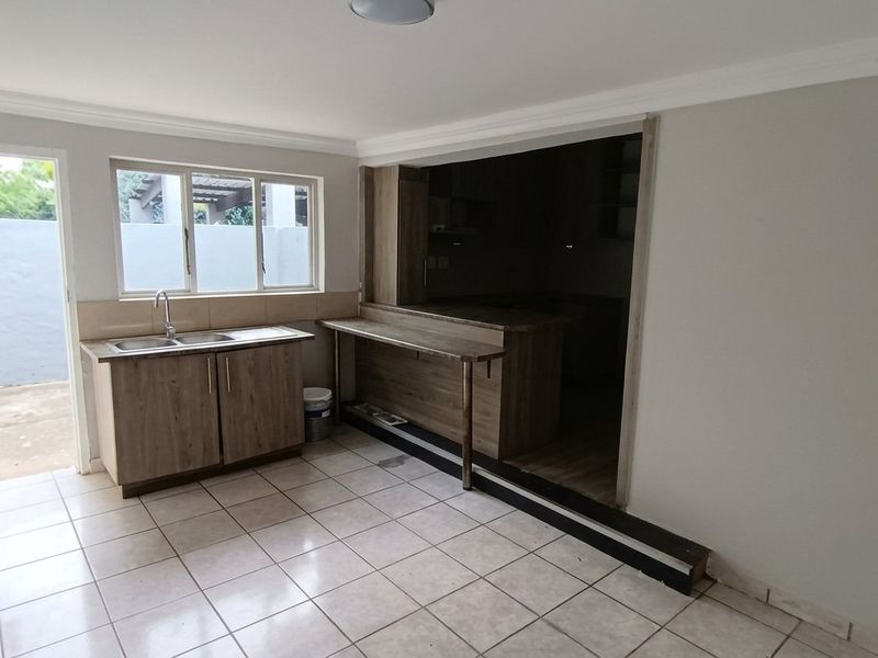 A functional kitchen area featuring tiled flooring, built-in cabinetry with a double sink, and a breakfast bar opening into an adjacent space.