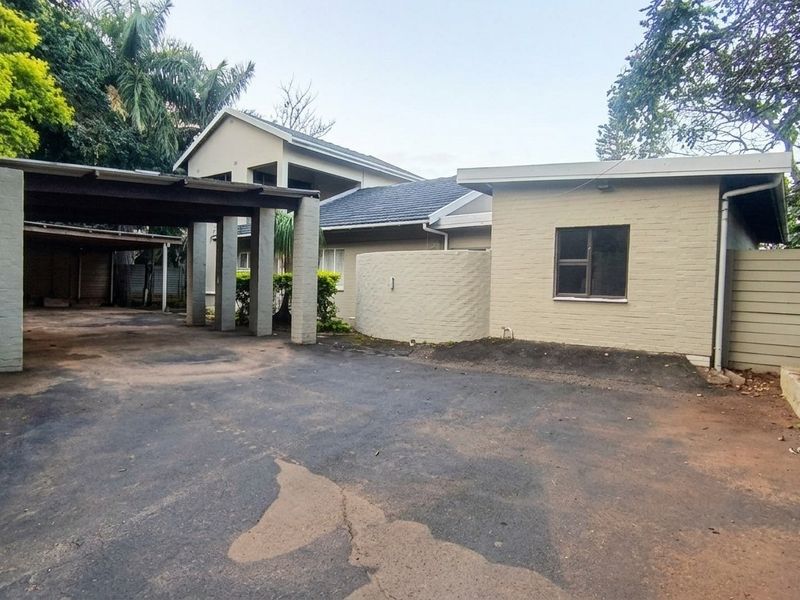 Front exterior view of the property featuring a spacious carport, brick facade, and an asphalt driveway with mature surrounding trees.
