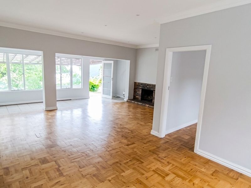 Spacious, light-filled living area featuring classic parquet flooring, a brick fireplace, and direct access to an outdoor patio through sliding glass doors.