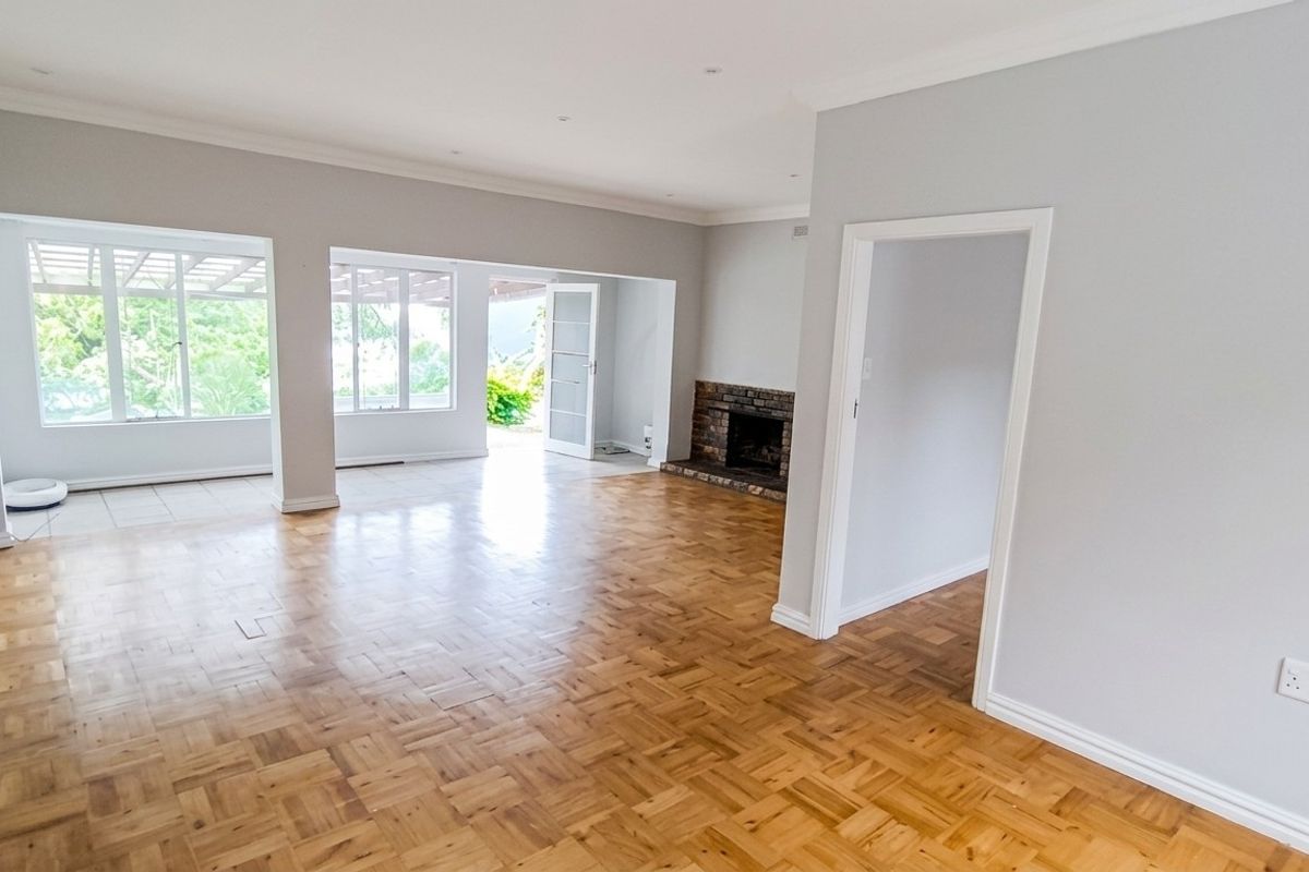 Spacious, light-filled living area featuring classic parquet flooring, a brick fireplace, and direct access to an outdoor patio through sliding glass doors.
