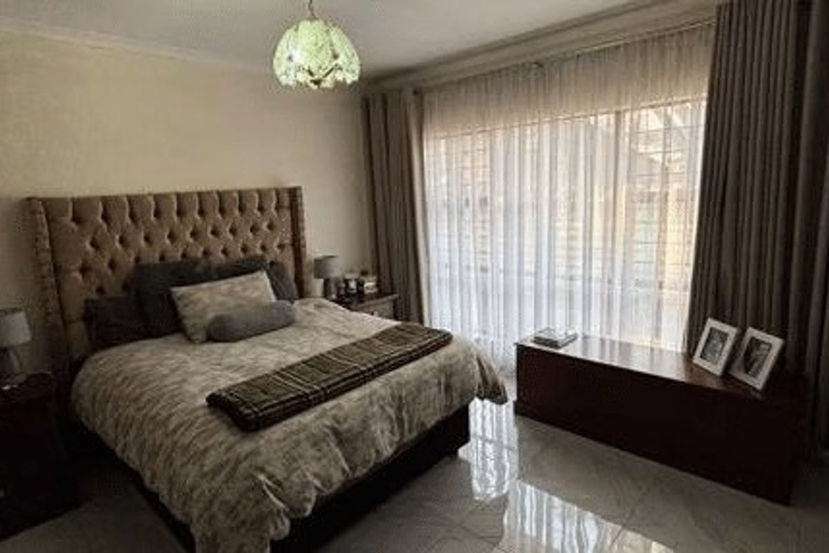 Spacious bedroom featuring polished tiled flooring, large window with curtain treatments, and a central ceiling light fixture.