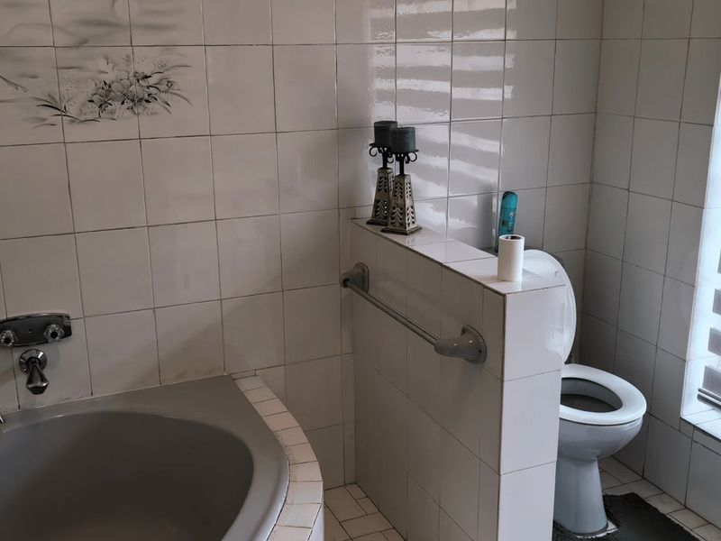 A functional bathroom featuring a built-in bathtub, toilet, and tiled finishes, complemented by a window with a roller blind.