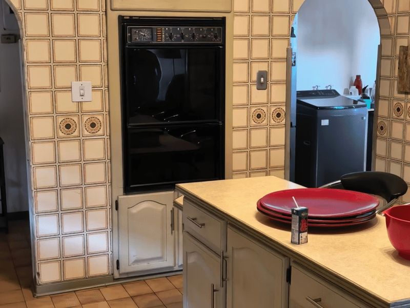 A dated kitchen featuring built-in double ovens, tiled wall finishes, and a central island, offering significant potential for a modern renovation.