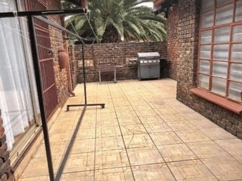 A paved outdoor patio area featuring exposed brick walls and sliding glass door access, providing a functional space for outdoor living.