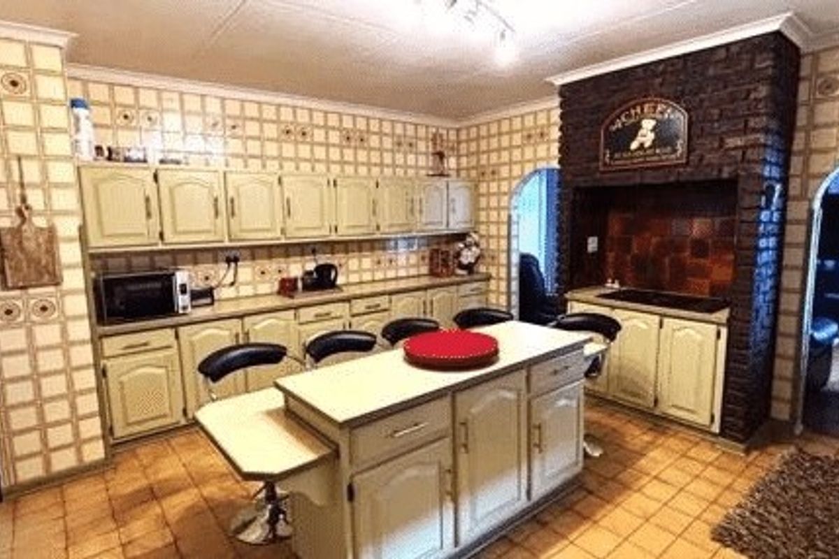 A spacious kitchen featuring a central island, extensive built-in cabinetry, and a distinctive brick feature wall with a built-in cooking area.