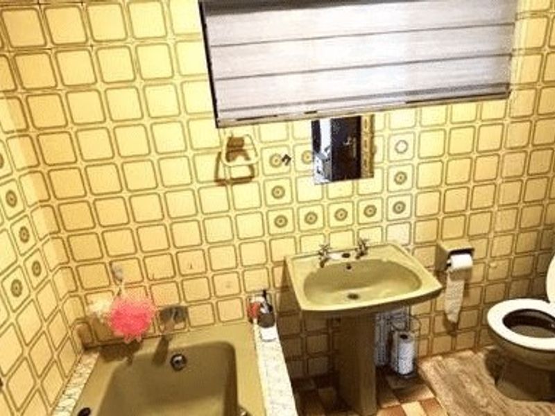 A dated bathroom featuring a pedestal sink, built-in bathtub, and toilet, finished with retro patterned wall tiles.