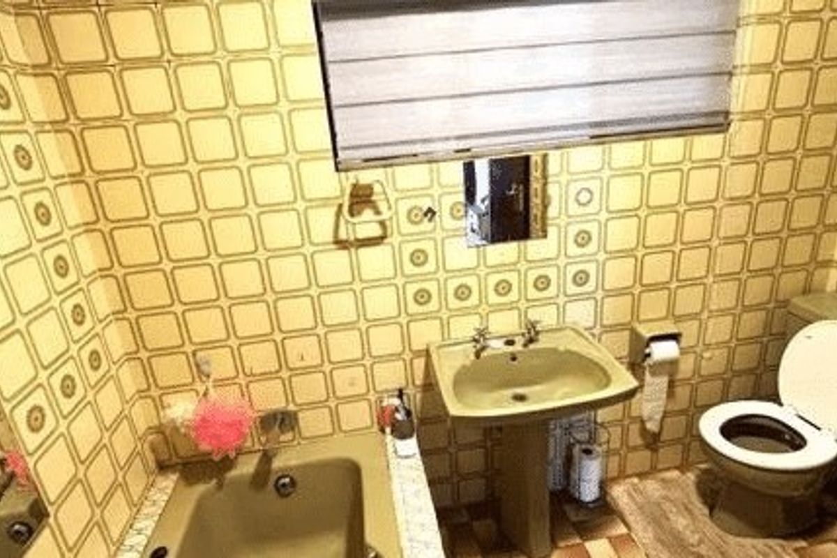 A dated bathroom featuring a pedestal sink, built-in bathtub, and toilet, finished with retro patterned wall tiles.