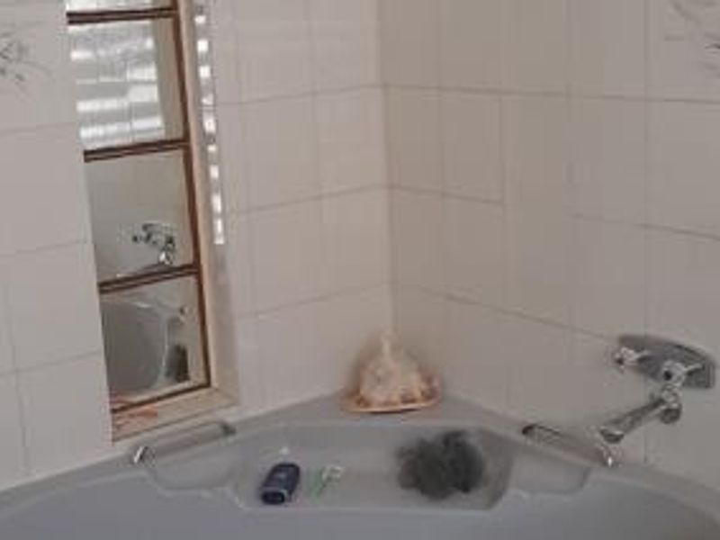 A corner bathtub featuring chrome fixtures and tiled walls, requiring minor maintenance and updates to modernize the space.
