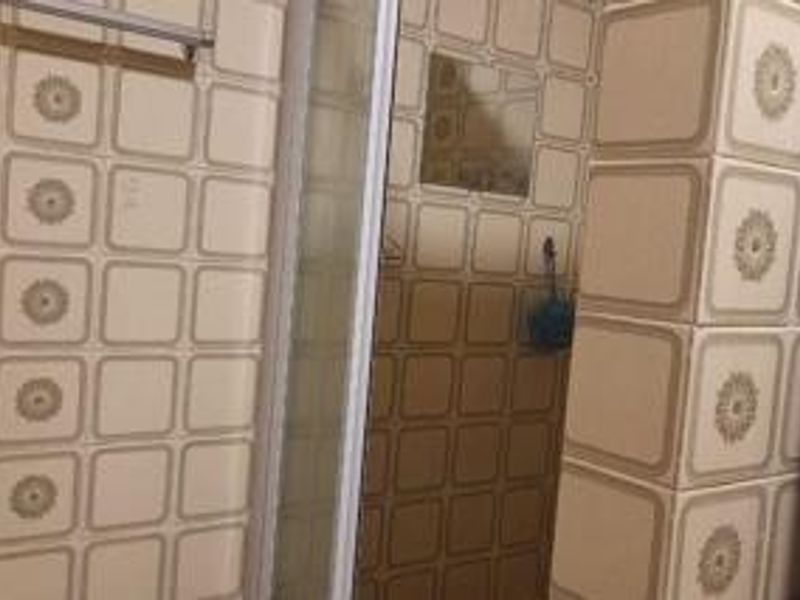 A bathroom featuring a shower enclosure and dated patterned wall tiles, presenting an opportunity for modernization and renovation.
