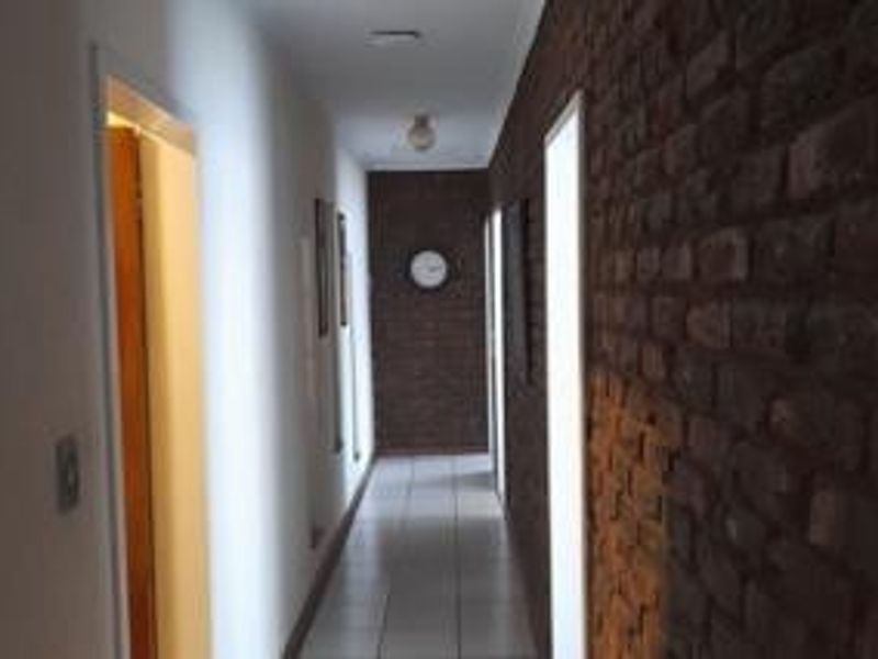 A long hallway featuring an exposed brick feature wall, tiled flooring, and multiple doorways leading to other rooms.