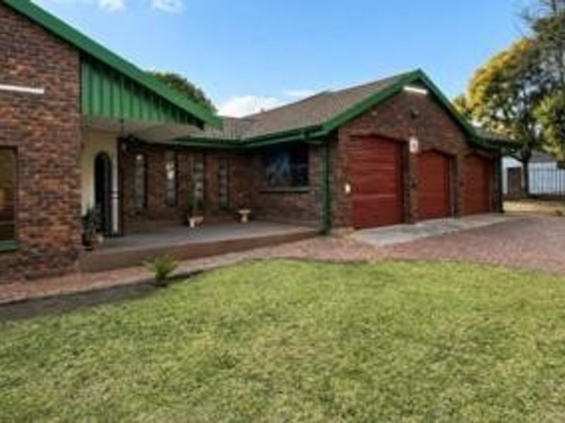 A well-maintained face brick house featuring a triple garage, a covered entrance porch, and a neat front lawn with a paved driveway.